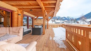 Une terrasse en bois avec un canapé et un coin repas donnant sur un paysage montagneux enneigé.