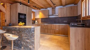 Une cuisine moderne avec des meubles en bois, un mur d’accent en pierre et un îlot central intégré avec des tabourets de bar.