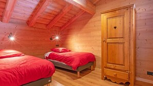 Une chambre dans un chalet en bois, avec deux lits, une armoire en bois et un plafond en pente.