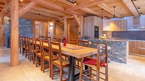 Un vaste espace de salle à manger avec une longue table et des chaises en bois, un mur d’accent en pierre et une cuisine équipée d’appareils électroménagers modernes.