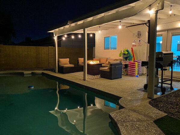A covered outdoor area with a pool, seating, and a grill.