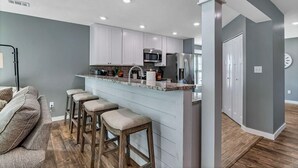 Una cocina moderna con armarios blancos, una isla central con taburetes y electrodomésticos de acero inoxidable.
