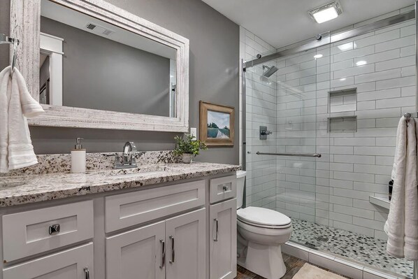 A modern bathroom with a granite countertop, a white toilet, and a glass shower enclosure.