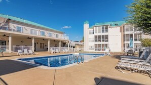 Zona de piscina con sillones de descanso y un edificio con tejado verde.
