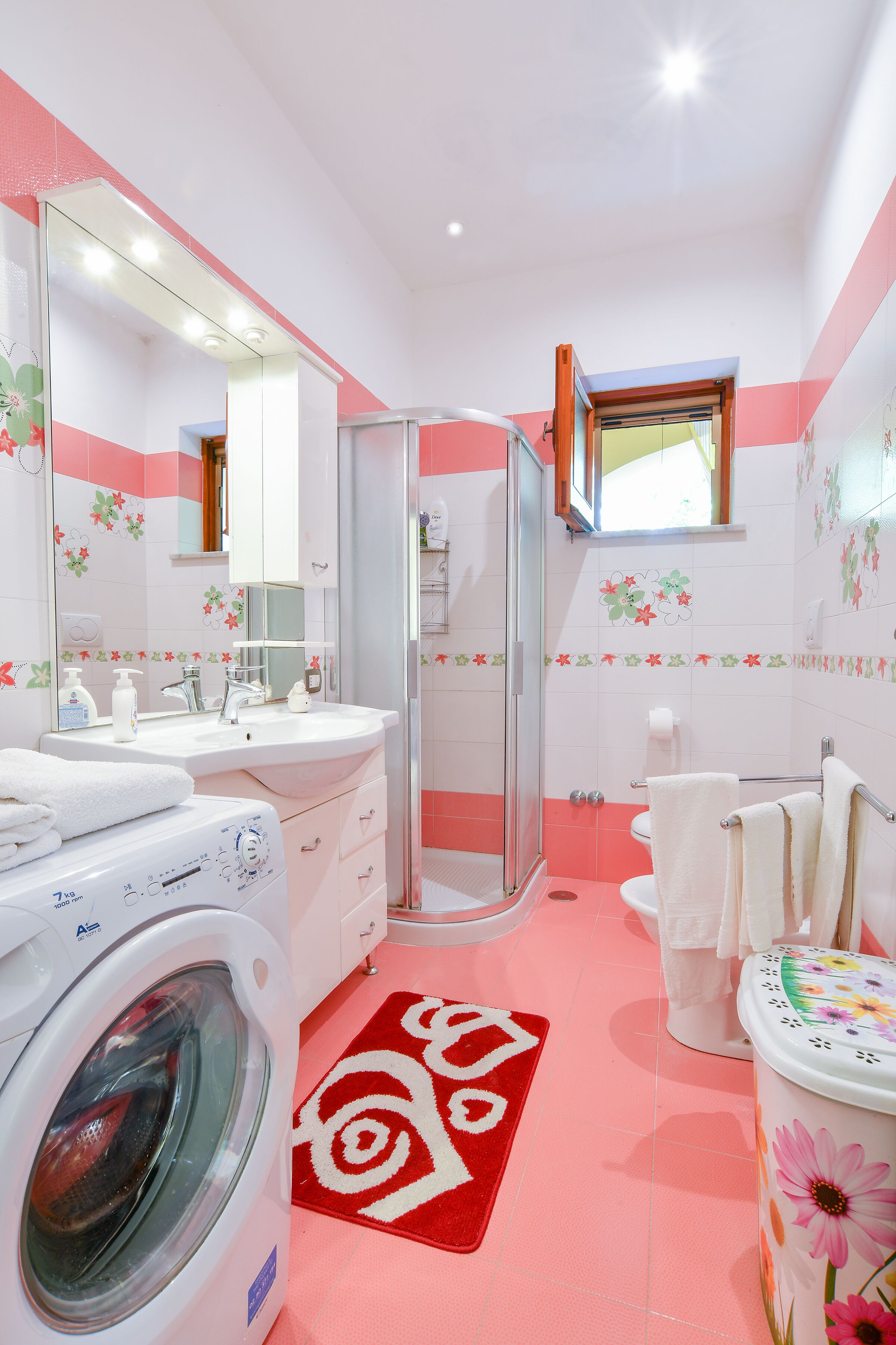 A bathroom with a washing machine, a glass shower enclosure, a toilet, and a sink.