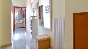 Un couloir avec un sol carrelé de carreaux blancs, un banc rembourré, un radiateur et une porte.