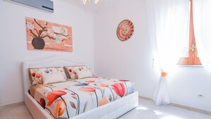 Une chambre à coucher avec un lit, un climatiseur fixé au mur et une fenêtre avec des rideaux.