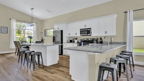 Une cuisine moderne avec des meubles blancs, un îlot central doté de tabourets, un réfrigérateur, un four à micro-ondes et une cuisinière.