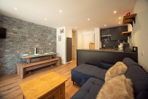 Un salon moderne avec un mur en pierre, un canapé foncé, une table basse en bois et un coin cuisine équipé d’un four à micro-ondes et de placards.
