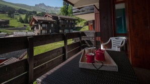 A balcony with a wooden railing, a table with a tray holding red pots, and a white chair. - 50m from ski slopes, 1st floor, view mountain, balcony, tv, ski locker, 34m², Valmorel (Valmorel)