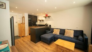 A modern living room with a dark blue sofa, wooden coffee table, and a kitchen area in the background. - 50m from ski slopes, 1st floor, view mountain, balcony, tv, ski locker, 34m², Valmorel (Valmorel)