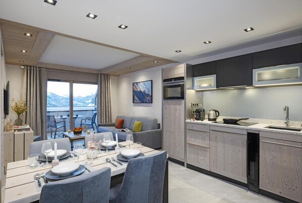 A modern kitchen with built-in appliances, a dining area with a table set for four, and a view of the mountains through large windows.