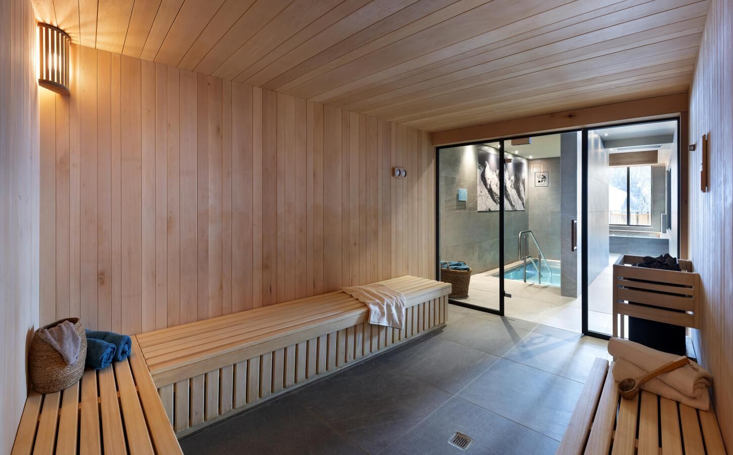 A sauna room with wooden benches, a glass door leading to a pool area, and a towel rack.
