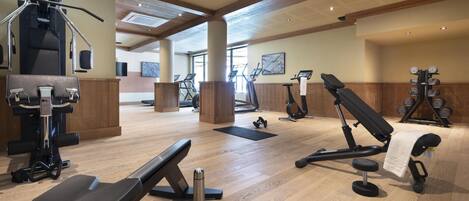 A gym with various exercise equipment, wooden flooring, and large windows allowing natural light.