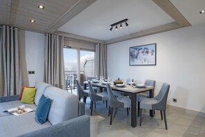 Un comedor moderno con una mesa dispuesta para cuatro, un sofá con cojines y un gran ventanal con cortinas.