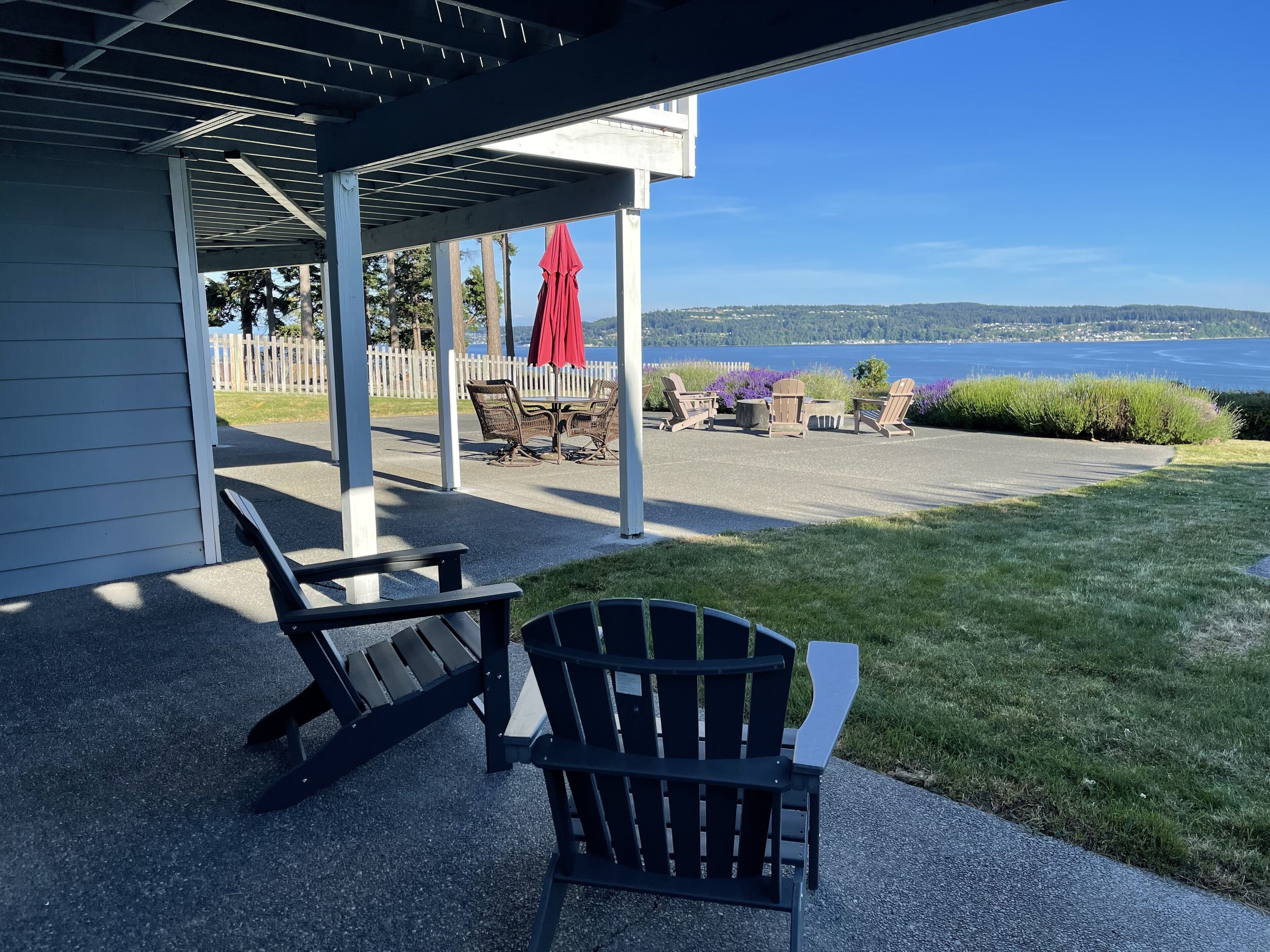 A covered patio with outdoor furniture, a view of the sea, and a white fence.