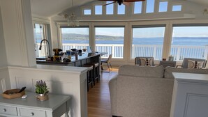 Une cuisine spacieuse avec un grand îlot central, un coin repas doté d’un canapé gris et une vue sur la mer grâce à de grandes fenêtres.