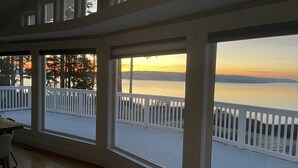 Une pièce dotée de grandes fenêtres donnant sur le bord de l’eau, avec une terrasse en bois et des balustrades blanches.