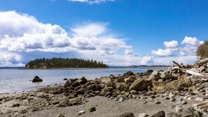 Une plage rocheuse avec, au loin, une île couverte de forêts.