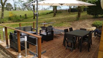 Une terrasse extérieure avec un revêtement de sol en bois, des meubles d’extérieur noirs et un grand parasol.