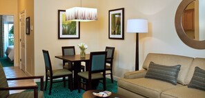 A hotel room with a dining table, chairs, a sofa, a lamp, and framed pictures on the wall. - Harborside at Atlantis with Water Park Amenities (Nassau)