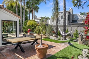 A patio with a wooden table, a potted tree, and a hammock.