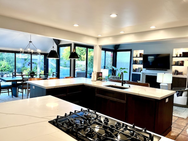 A modern kitchen with a large island, a gas stove, and a dining area with a table and chairs.