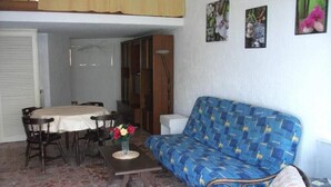 Una sala acogedora con un sofá azul estampado, una mesa de comedor con sillas y una pequeña mesa de centro con flores.