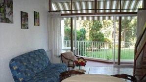 Una habitación con un sofá azul, una mesita con un jarrón de flores y un balcón con vistas a la vegetación.