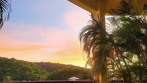A round metal table with chairs, a wooden railing, and a view of a lush green landscape during sunset. - Huatulco beauty in Chahue Bay. Large family condo with ocean and mountain views (Chahue)