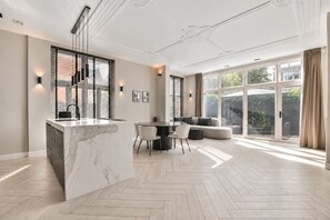 A modern kitchen with a marble island, a dining area with a table and chairs, and a large sliding glass door leading to a garden.