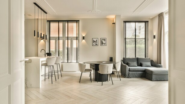 A modern living room with a grey sectional sofa, a round dining table with four chairs, and a kitchen area with a bar counter and pendant lights. - Luxury Rijksmuseum house (Amsterdam)