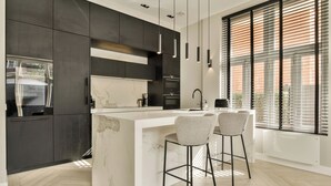 A modern kitchen with dark cabinetry, a marble island, and pendant lighting. - Luxury Rijksmuseum house (Amsterdam)