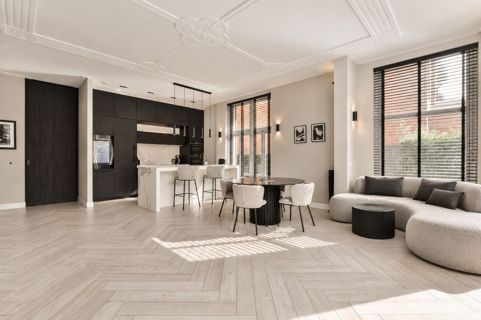 A spacious living area with a large sofa, a dining table with chairs, and a kitchen area with dark cabinets and a white countertop.