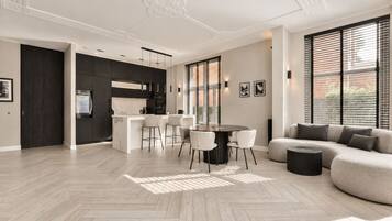 A spacious living area with a large sofa, a dining table with chairs, and a kitchen area with dark cabinets and a white countertop.