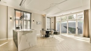 A spacious kitchen with a marble island, a dining area with a round table and chairs, and large windows with curtains. - Luxury Rijksmuseum house (Amsterdam)