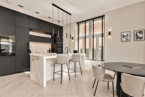 A modern kitchen with a marble island, bar stools, and a dining table with chairs.