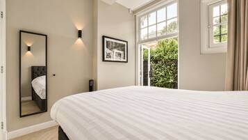 A bedroom with a large bed, a bedside mirror, a wall-mounted light, and a window with curtains.