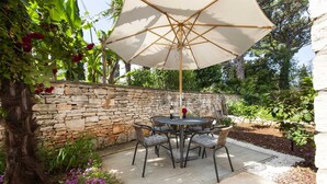 A stone wall, a round table with chairs, and an umbrella in a garden setting. - KATARINA One-Bedroom Apartment with Terrace 2 (Rovinj)