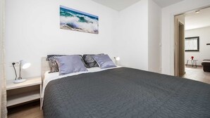 A bedroom with a bed, a nightstand, a lamp, and a painting of a beach scene. - KATARINA One-Bedroom Apartment with Terrace 2 (Rovinj)