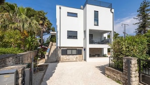 A modern two-story building with a white facade, a balcony on the upper floor, and a gravel driveway leading to the entrance.