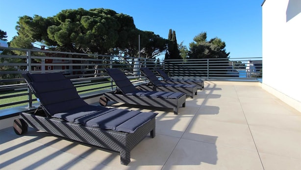 A rooftop terrace with sun loungers and a pool in the background.