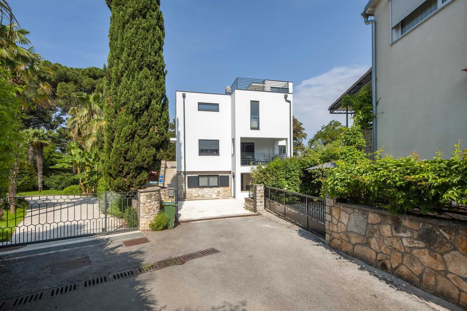 Un edificio moderno de dos pisos con fachada de piedra, entrada con portón y cielo despejado.