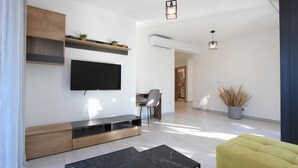 A modern living room with a flat-screen TV, wooden shelves, a dining area, and a yellow sofa.