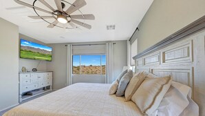 Ein Schlafzimmer mit einem großen Bett, einem Deckenventilator, einem an der Wand montierten Fernseher und einem Fenster mit Blick auf die Wüste.