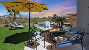 Eine Terrasse mit Feuerstelle, Liegestühlen und einem gelben Sonnenschirm.