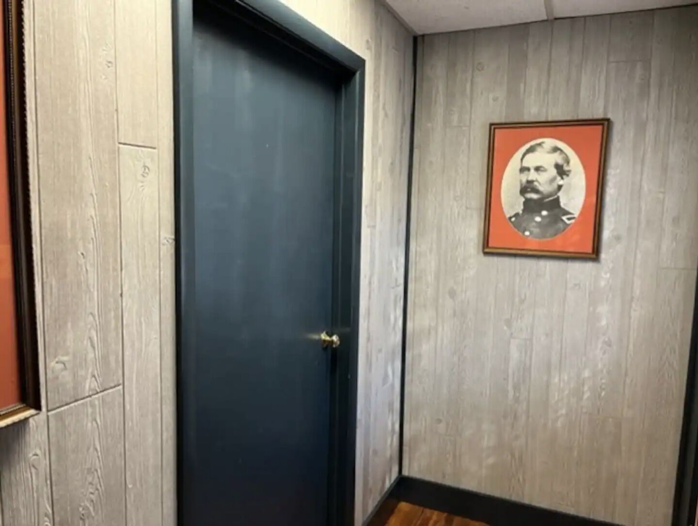 A room with a dark blue door, a framed picture on the wall, and a wooden floor.