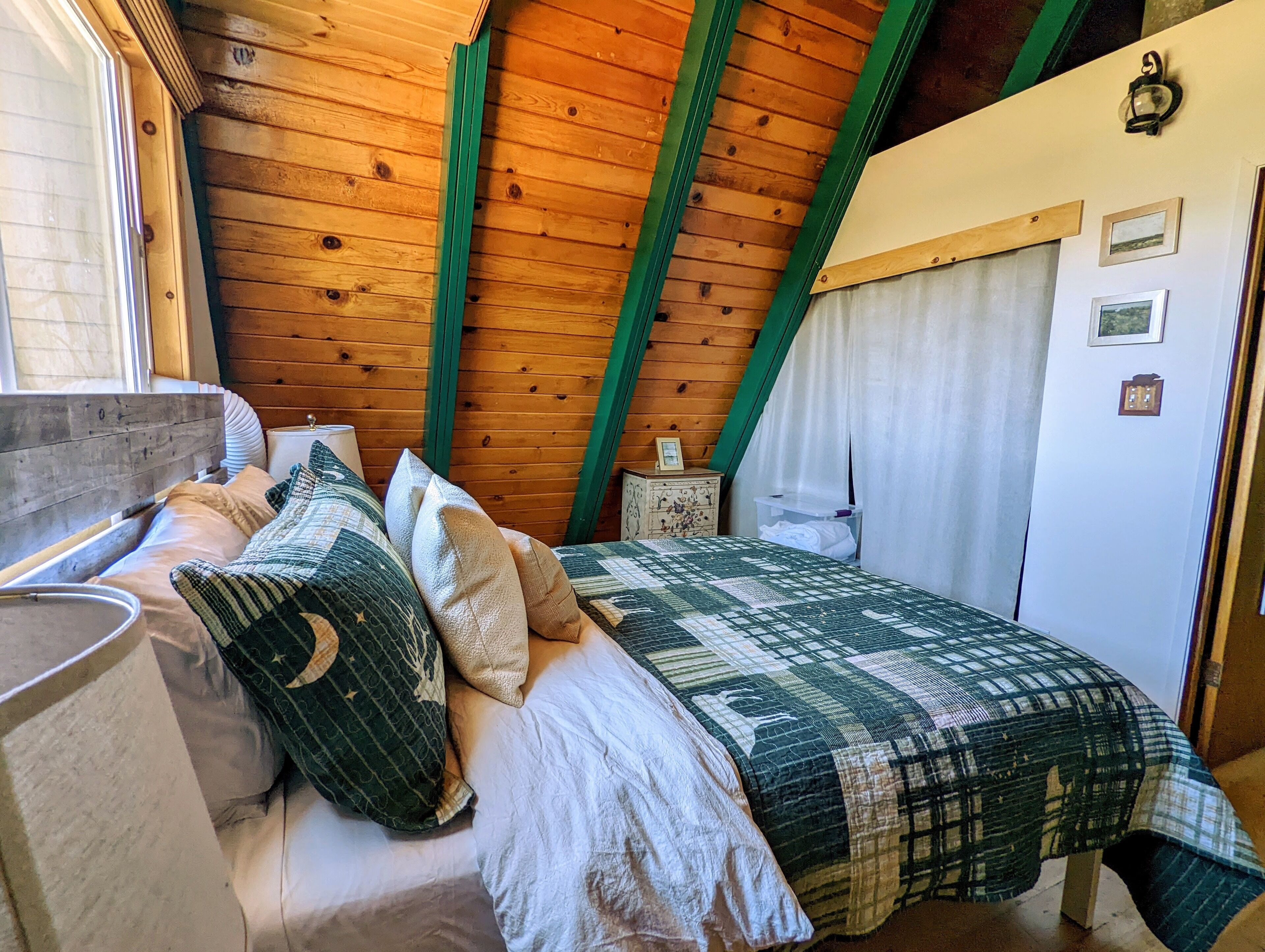 Una camera accogliente con soffitto in legno, un letto con biancheria a motivi, un comodino e una finestra con tende.