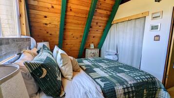 Una camera accogliente con soffitto in legno, un letto con biancheria a motivi, un comodino e una finestra con tende.