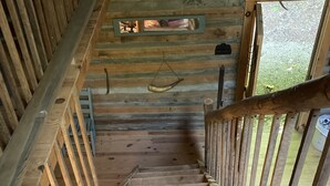 A wooden staircase with a metal handrail, leading to a room with a wooden ceiling and a window. - Retreat with rustic cabin, picnic shed and ponds (Leicester)